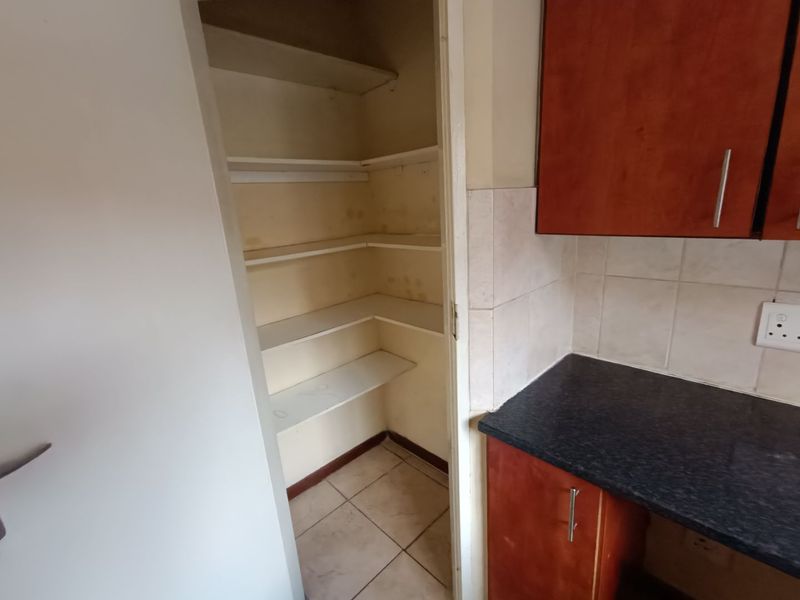 A small walk-in pantry or scullery area featuring built-in shelving, adjacent to a kitchen space with laminate cabinetry and tiled splashback.