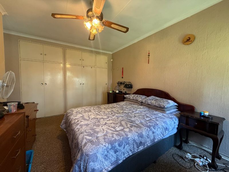 A bedroom featuring built-in cupboards, a ceiling fan, and carpeted flooring, offering a functional space with potential for cosmetic updates.