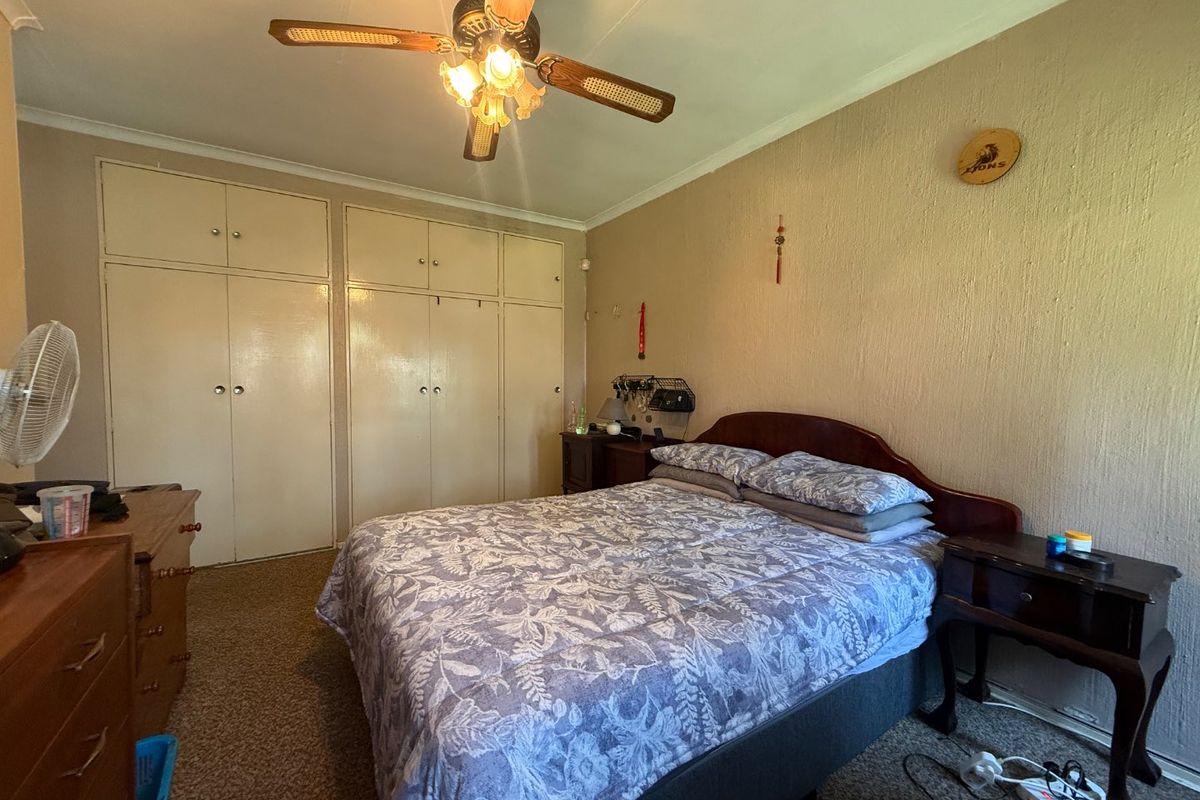 A bedroom featuring built-in cupboards, a ceiling fan, and carpeted flooring, offering a functional space with potential for cosmetic updates.