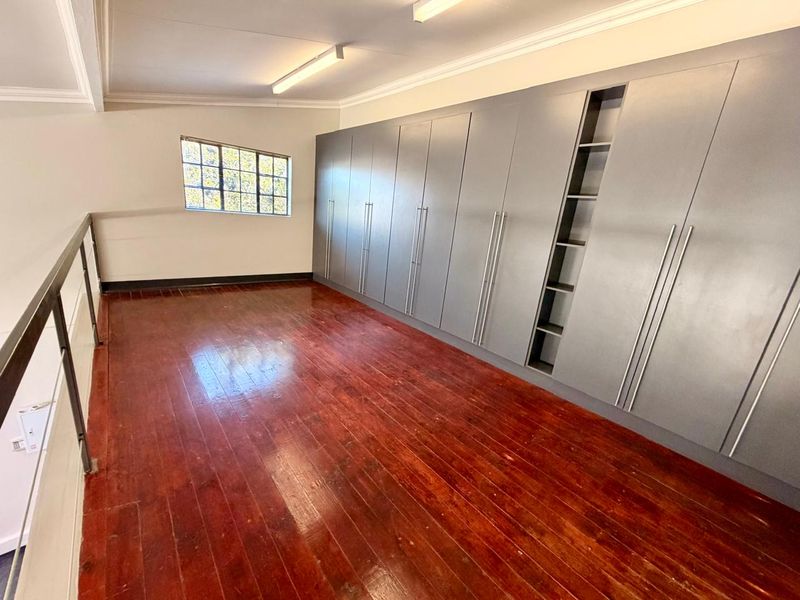 An open-plan loft space featuring polished hardwood flooring, extensive built-in grey cabinetry, and a metal balustrade overlooking the lower level.
