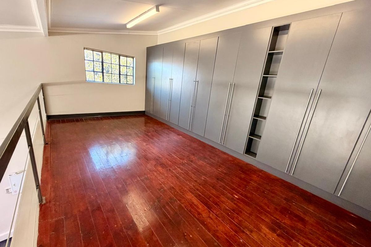 An open-plan loft space featuring polished hardwood flooring, extensive built-in grey cabinetry, and a metal balustrade overlooking the lower level.