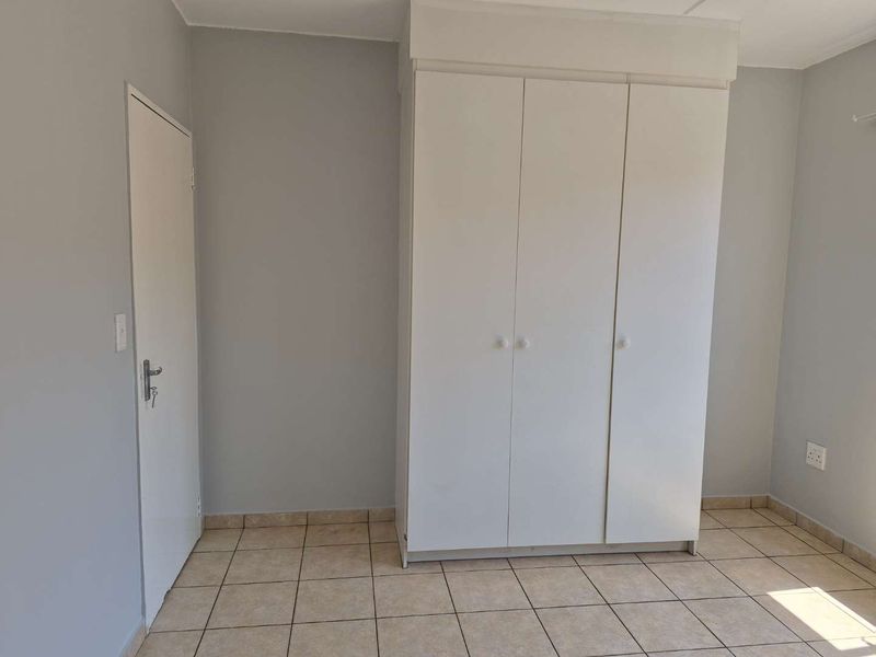 A clean, empty bedroom featuring neutral grey walls, tiled flooring, and a white built-in wardrobe.