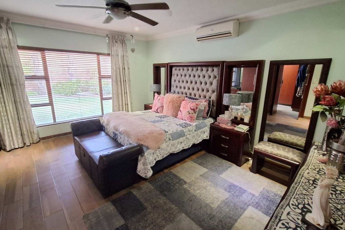 Spacious bedroom featuring tiled flooring, a ceiling fan, and a wall-mounted air conditioning unit, with large windows providing natural light.