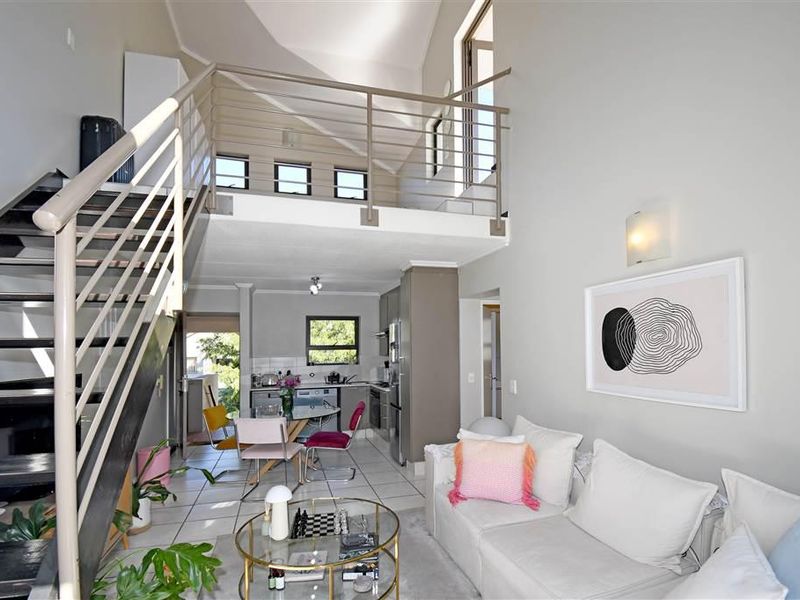 Open-plan living area featuring a mezzanine level, metal staircase, tiled flooring, and a functional kitchen space with high vaulted ceilings.