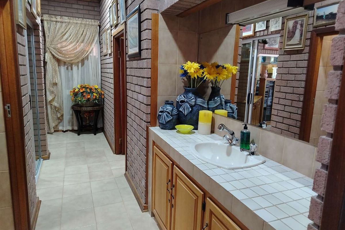 A bathroom featuring a tiled vanity countertop with a built-in sink, wooden cabinetry, and exposed brick walls.