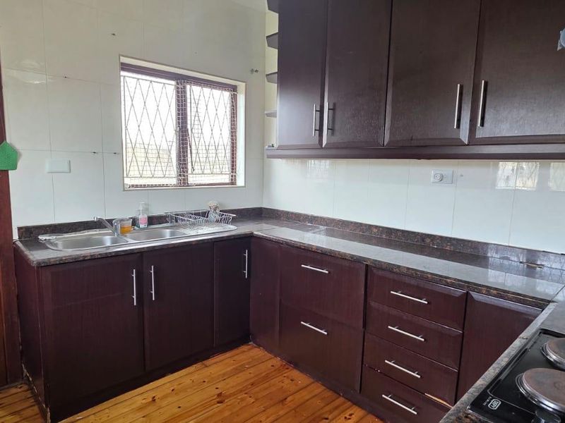 A functional kitchen featuring dark wood cabinetry, granite countertops, a double basin sink, and an electric hob with an extractor fan.