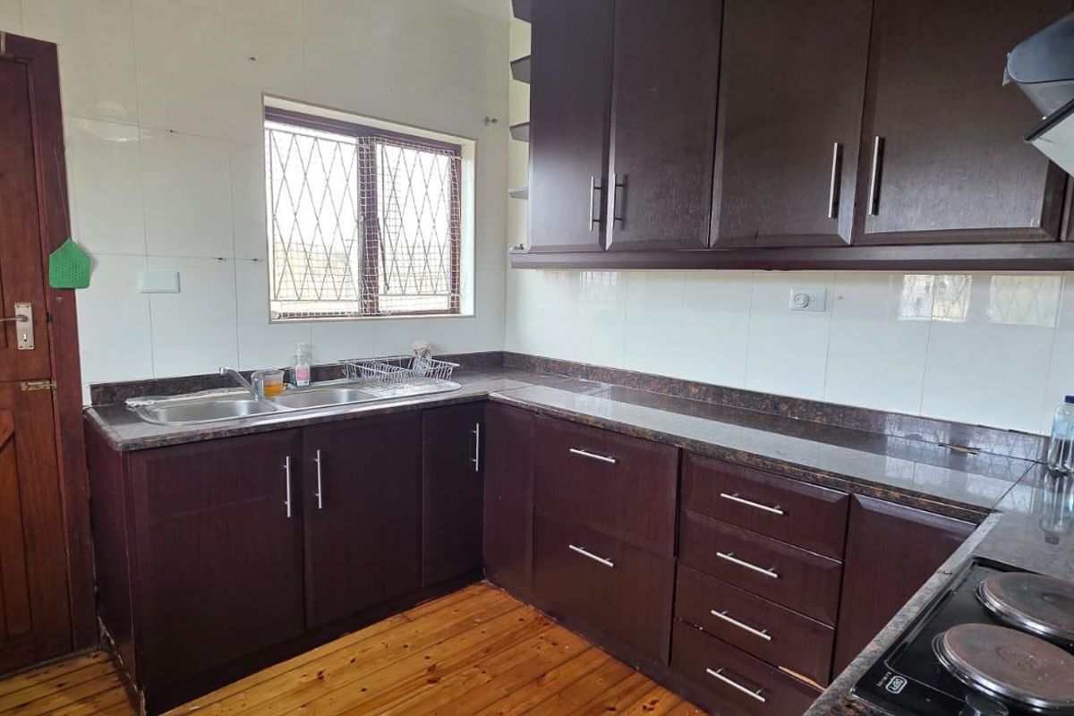 A functional kitchen featuring dark wood cabinetry, granite countertops, a double basin sink, and an electric hob with an extractor fan.