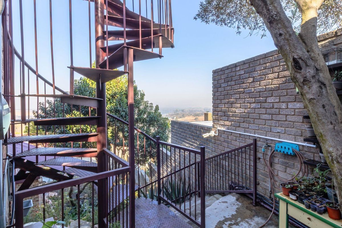 Exterior rear area featuring a metal spiral staircase, brick retaining walls, and metal safety railings with views of the surrounding landscape.
