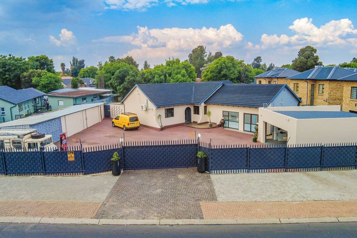 Aerial view of a well-maintained single-story house featuring a tiled roof, expansive paved driveway, and secure perimeter fencing with an automated gate.