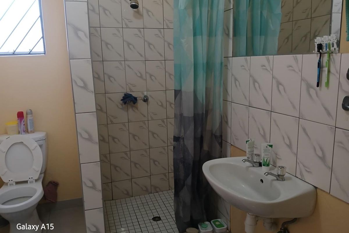 A functional bathroom featuring a tiled shower enclosure, wall-mounted basin, and toilet, with neutral wall finishes and a window for natural light.