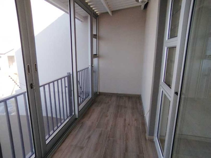 A clean, covered balcony featuring wood-look tile flooring, sliding glass doors, and a metal balustrade, offering a bright and functional outdoor space.