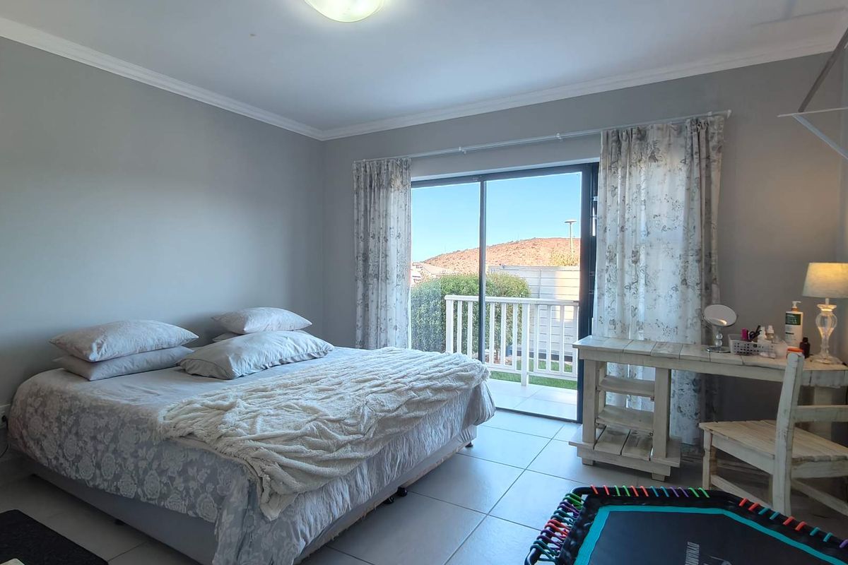A bright bedroom featuring tiled flooring, neutral walls, and sliding glass doors that open onto a private balcony with scenic views.