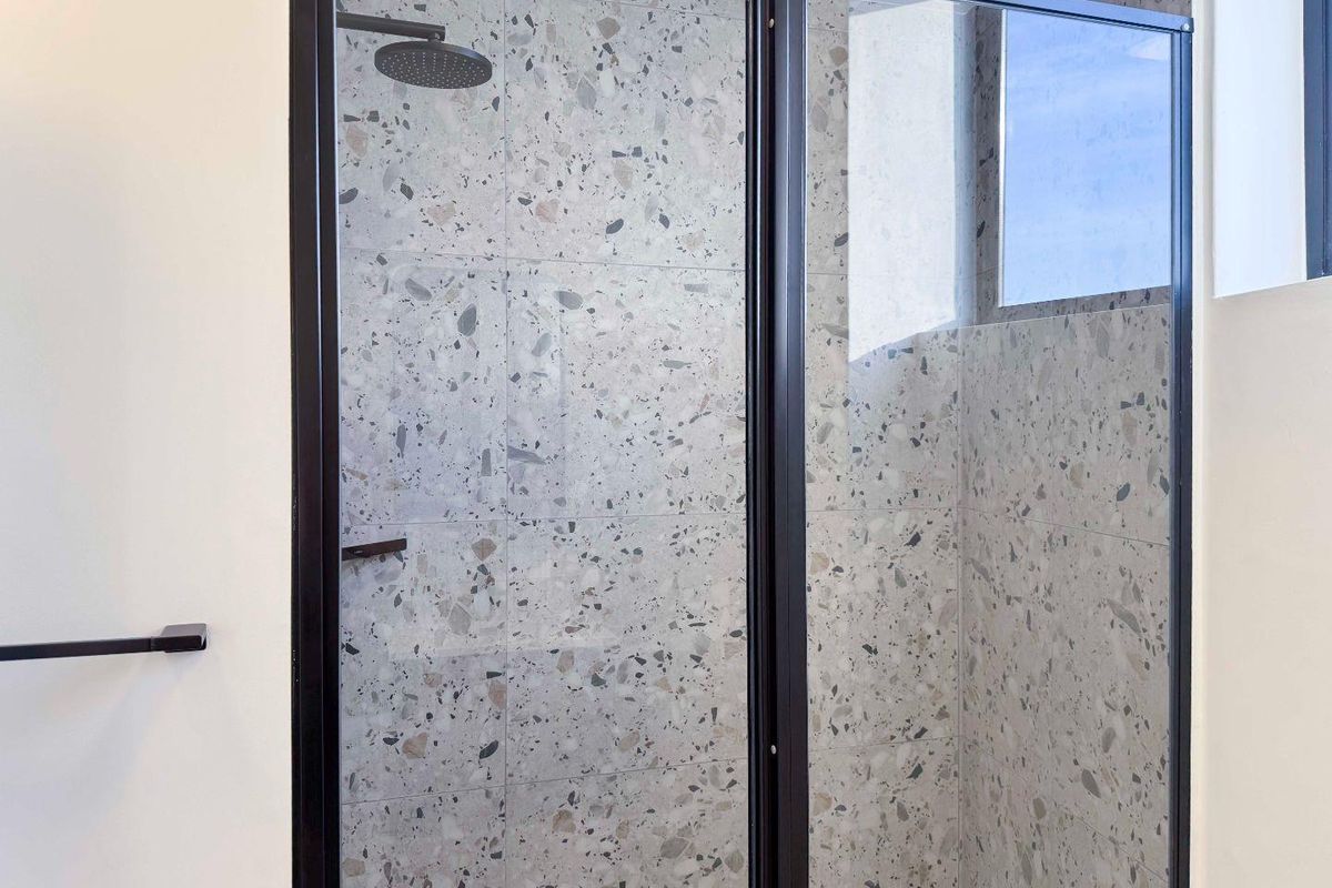 Modern bathroom shower featuring stylish terrazzo-style wall tiles, a sleek black-framed glass enclosure, and a contemporary rain shower head.