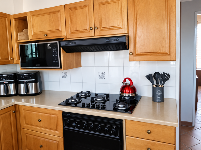 A functional kitchen featuring warm-toned wooden cabinetry, a black gas hob with integrated oven, extractor fan, and a tiled backsplash.