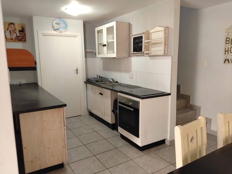Compact kitchen featuring built-in cabinetry, an integrated oven and hob, tiled backsplash, and tiled flooring, adjacent to a staircase.
