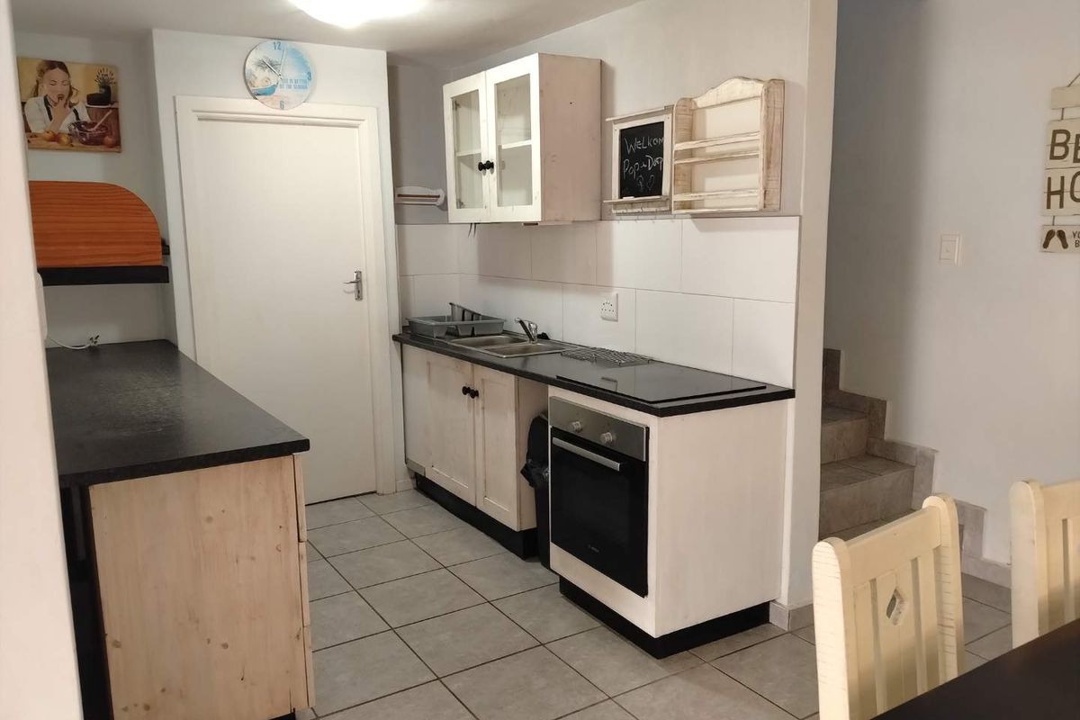 Compact kitchen featuring built-in cabinetry, an integrated oven and hob, tiled backsplash, and tiled flooring, adjacent to a staircase.
