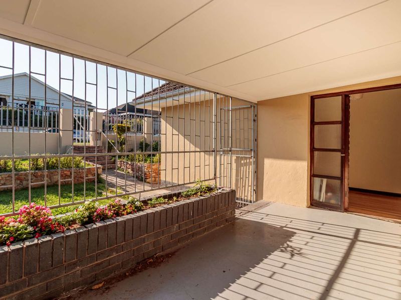 A covered patio area featuring a built-in brick planter box, security bars, and direct access to the interior through a timber-framed glass door.