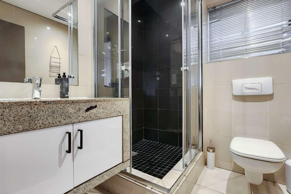 Modern bathroom featuring a granite vanity, wall-mounted toilet, and a glass-enclosed shower with contrasting dark tile accents.