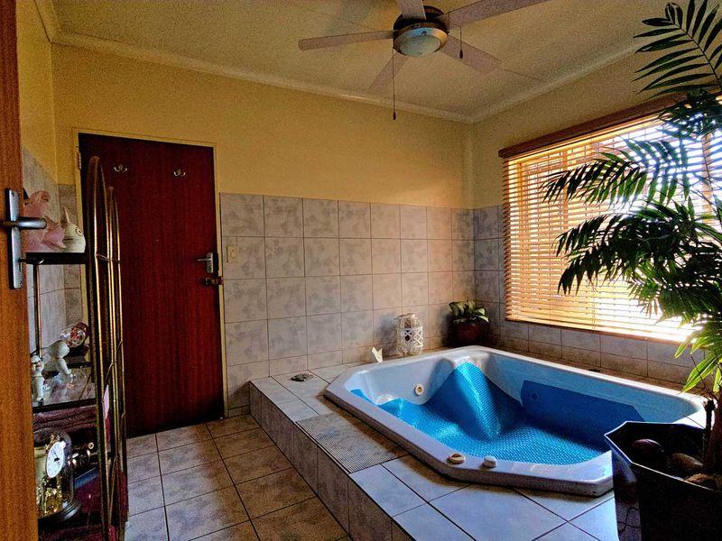 A bathroom featuring a built-in corner bathtub, tiled walls and flooring, and a ceiling fan, offering a functional space with potential for modern updates.