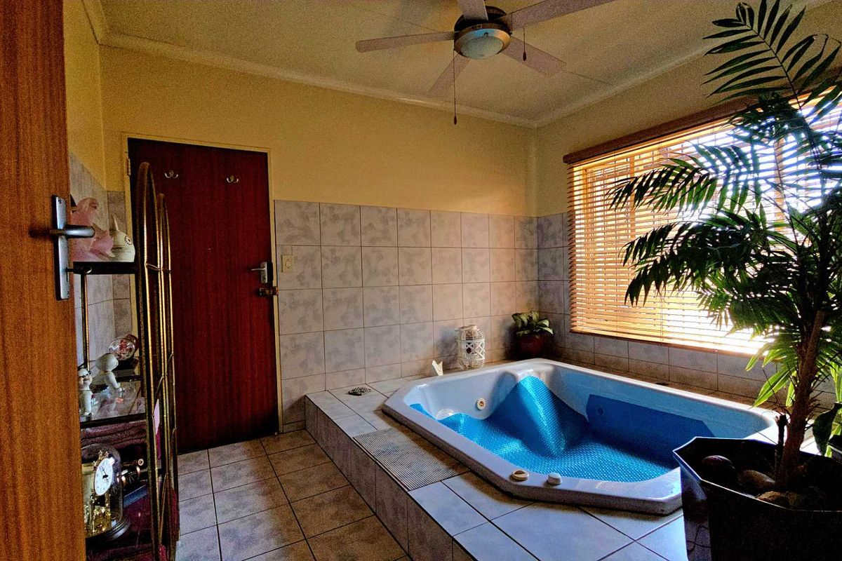 A bathroom featuring a built-in corner bathtub, tiled walls and flooring, and a ceiling fan, offering a functional space with potential for modern updates.
