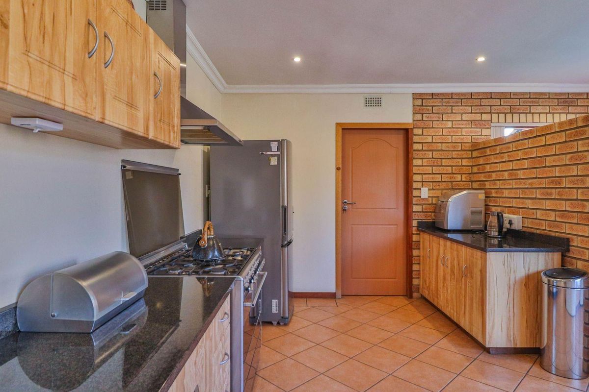 A functional kitchen featuring wooden cabinetry, granite countertops, a gas stove with extractor fan, and a distinctive exposed brick feature wall.