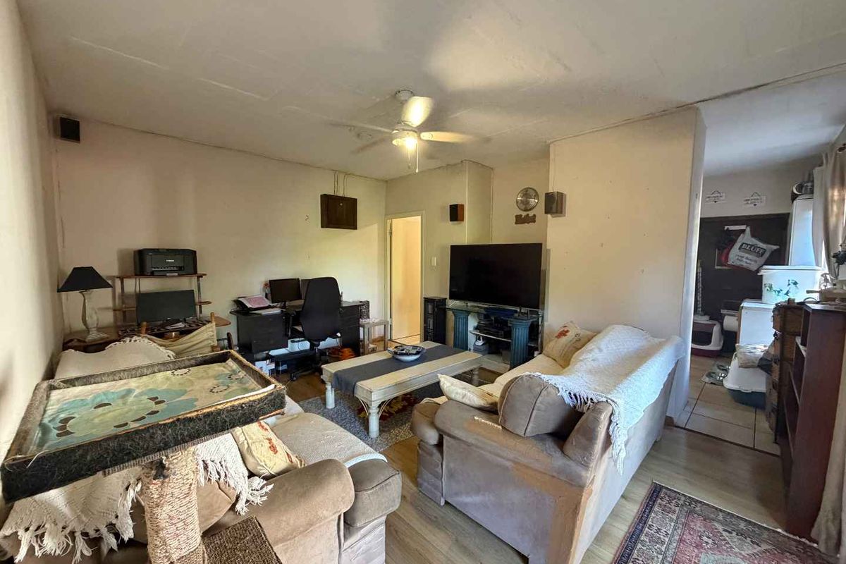 A living room area featuring laminate flooring, a ceiling fan, and direct access to an adjacent utility space.