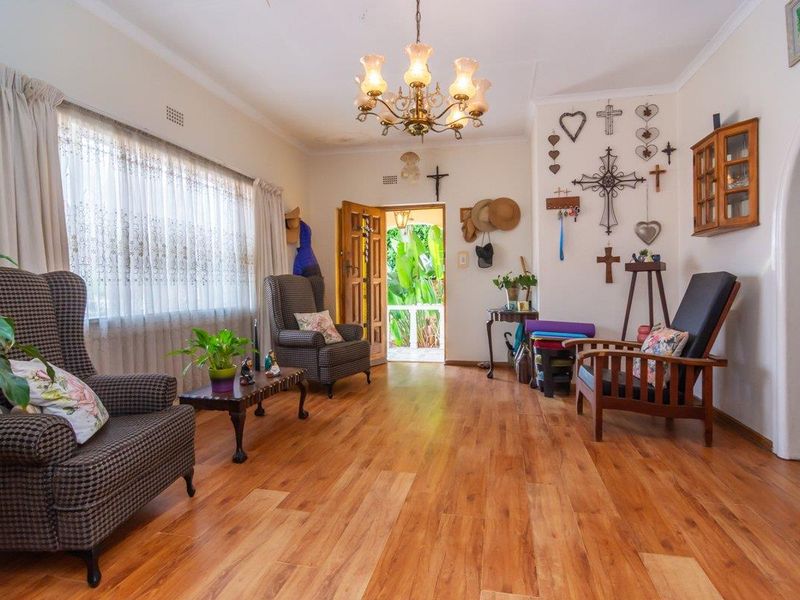 A bright living room featuring warm-toned laminate flooring, a classic chandelier, and an arched doorway leading to the exterior.