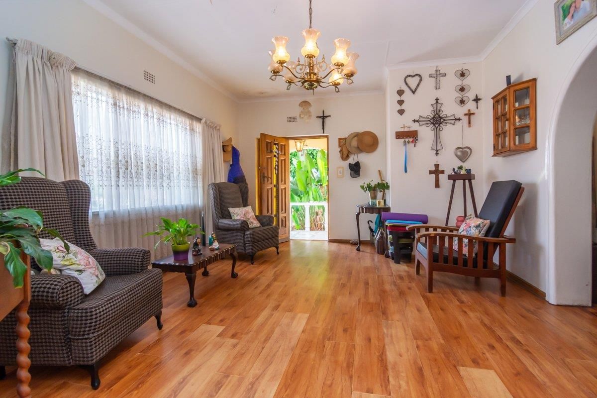 A bright living room featuring warm-toned laminate flooring, a classic chandelier, and an arched doorway leading to the exterior.