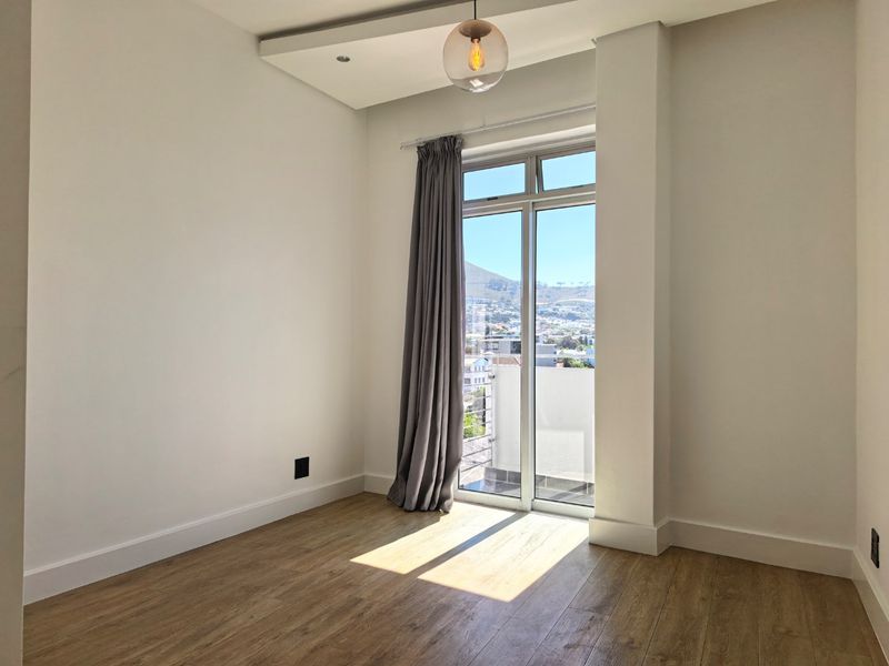 A bright, empty bedroom featuring modern laminate flooring, recessed ceiling lighting, and a glass sliding door providing access to a balcony with scenic views.