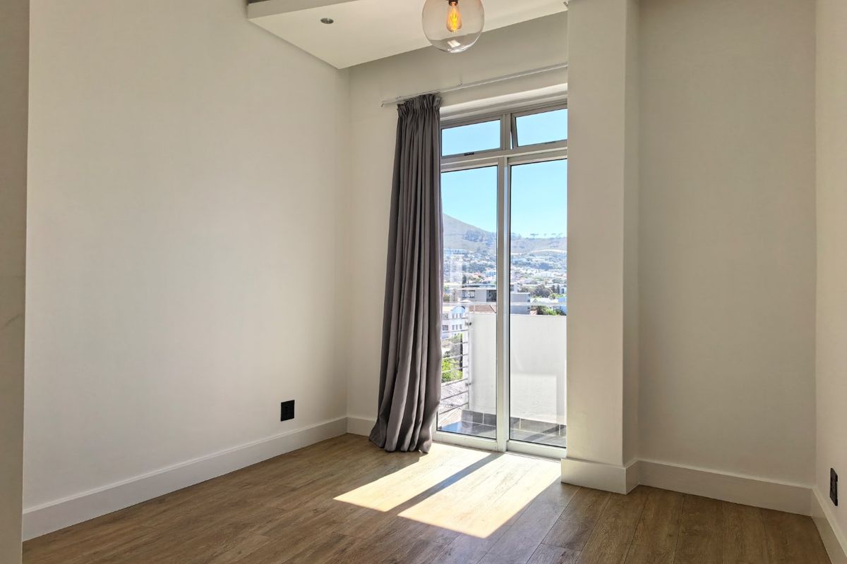 A bright, empty bedroom featuring modern laminate flooring, recessed ceiling lighting, and a glass sliding door providing access to a balcony with scenic views.