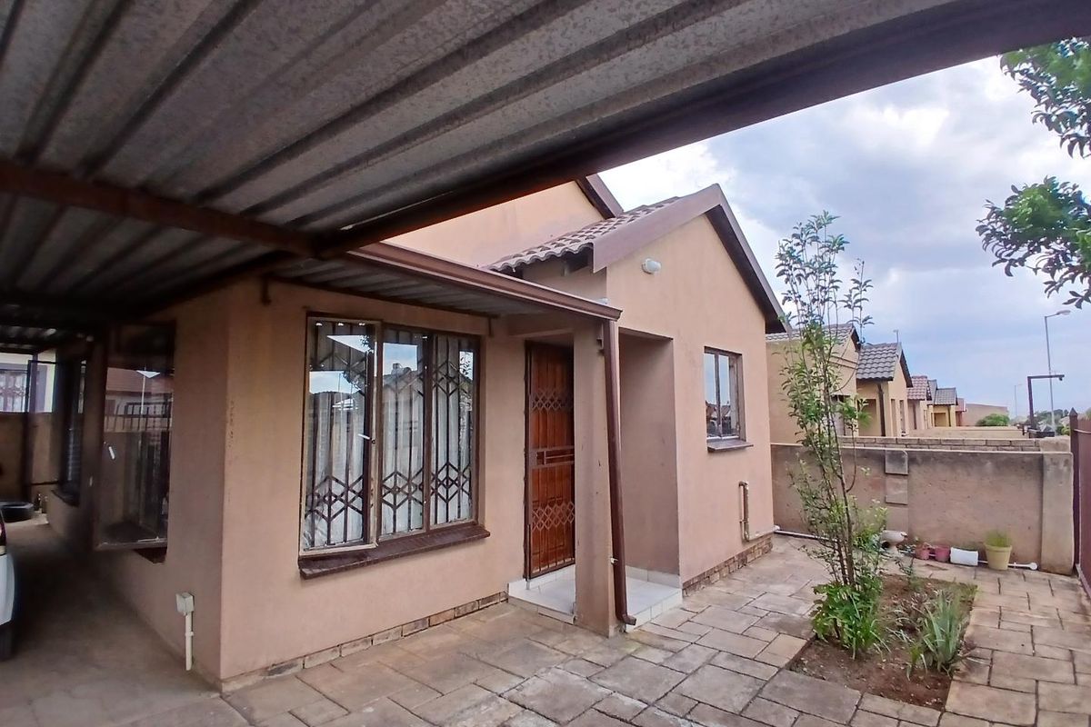 Exterior view of the house featuring a paved patio area, metal carport, and security gates on windows and doors.