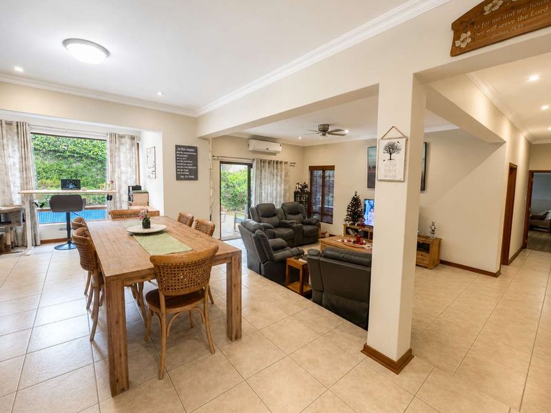 Spacious open-plan living and dining area featuring neutral ceramic floor tiles, crown molding, and direct access to the outdoor patio through sliding glass doors.