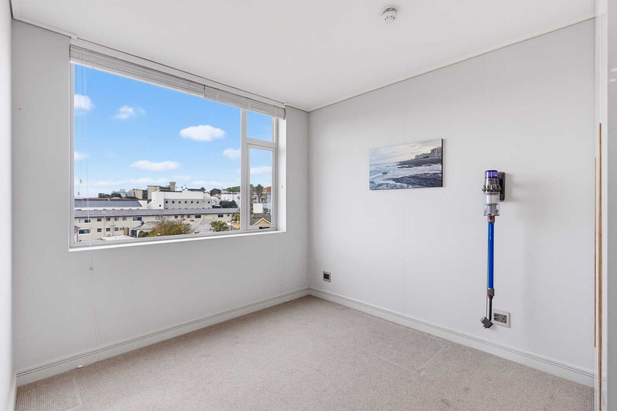 A bright, empty bedroom featuring neutral carpeting, a large window with urban views, and clean white walls.