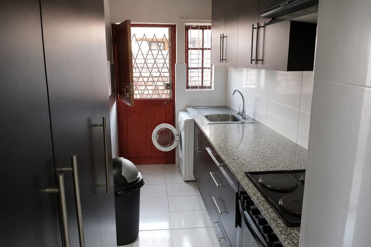 Compact scullery featuring dark cabinetry, granite countertops, a stainless steel sink, and an integrated electric hob with an extractor fan.