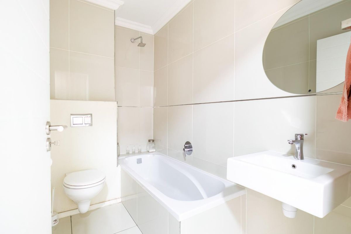 A clean, modern bathroom featuring a wall-mounted toilet, a built-in bathtub with a shower head, and a wall-hung vanity basin.
