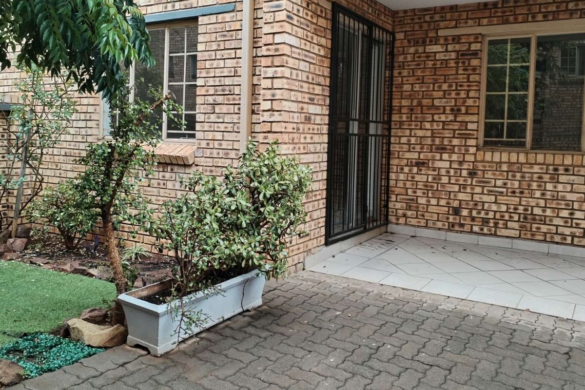 A rear exterior view of the apartment featuring a face brick facade, a tiled patio area, and a paved outdoor space.
