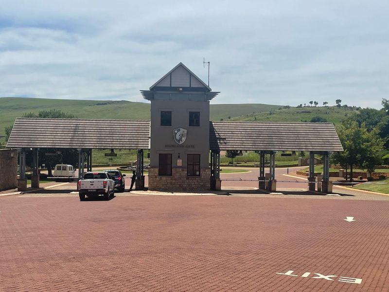 The main entrance gatehouse of Highland Gate estate, featuring a stone-clad structure, tiled roof, and controlled access boom gates.