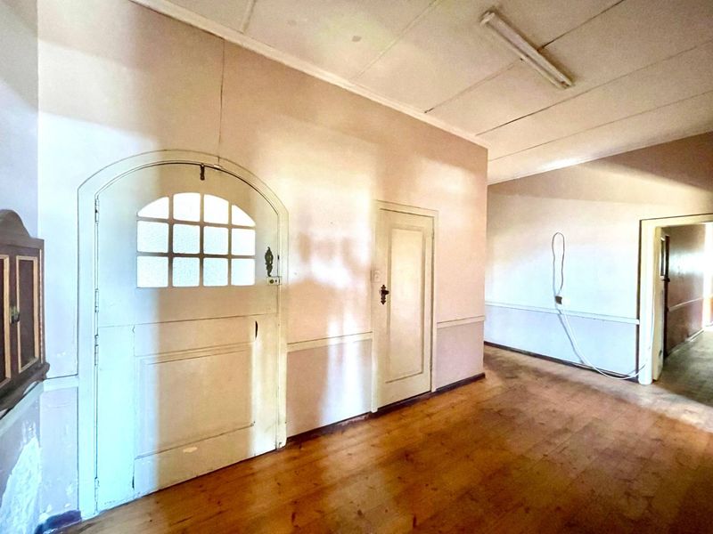 A vacant hallway featuring original timber flooring, panelled doors, and an arched entrance door, requiring cosmetic updates to restore its character.