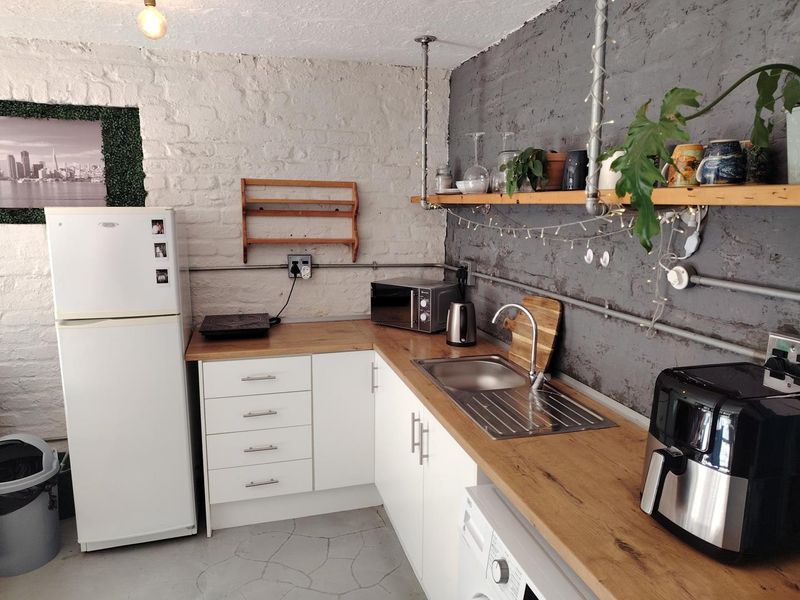 Compact kitchen featuring white cabinetry, wood-look laminate countertops, exposed brick walls, and industrial-style open shelving with exposed conduit electrical work.