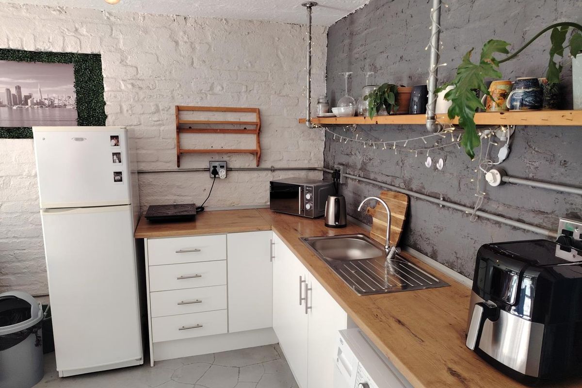 Compact kitchen featuring white cabinetry, wood-look laminate countertops, exposed brick walls, and industrial-style open shelving with exposed conduit electrical work.