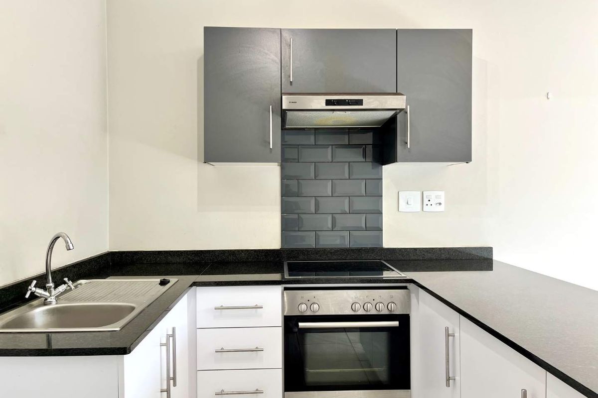 Modern kitchen featuring granite countertops, subway tile backsplash, built-in oven, electric hob, extractor fan, and ample white and grey cabinetry.