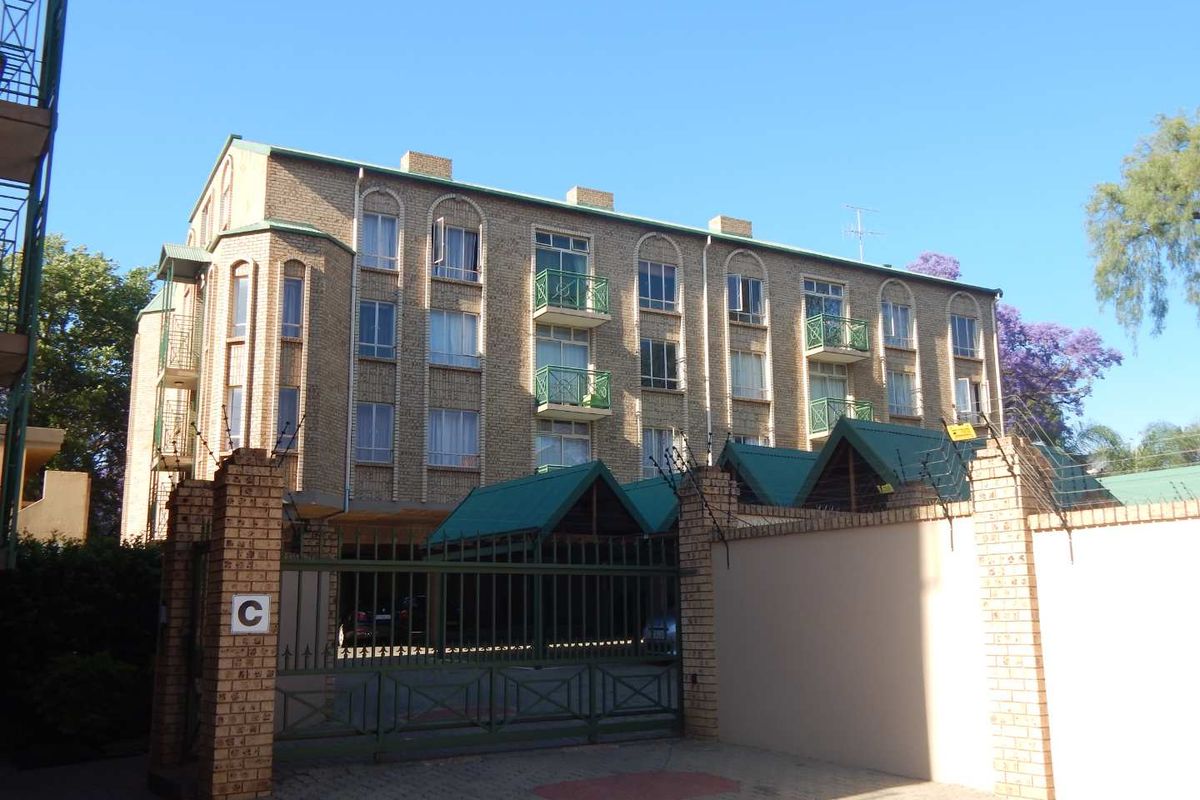 Front view of a multi-story brick apartment building featuring secure gated access, electric fencing, and private balconies.