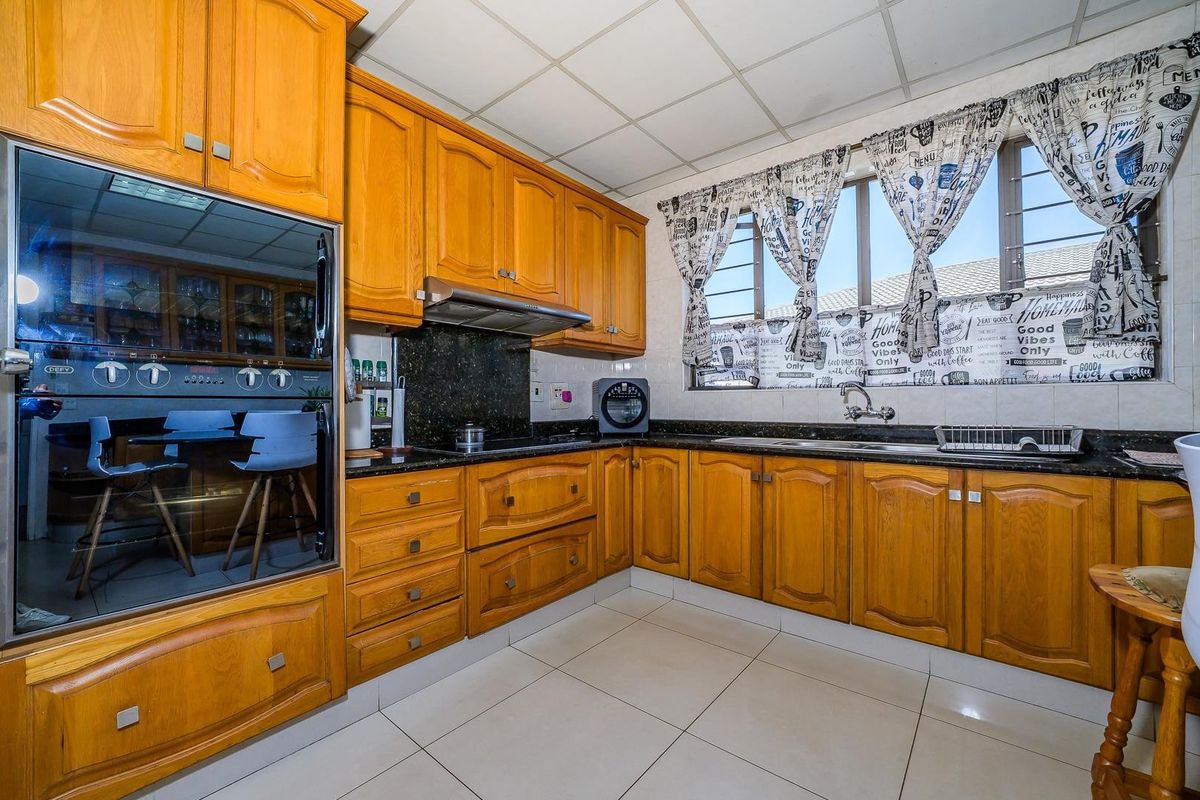 A functional kitchen featuring traditional wooden cabinetry, granite countertops, a built-in oven, and an extractor fan, with tiled flooring and a drop ceiling.