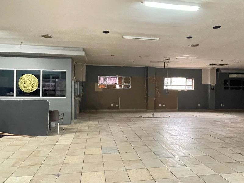 A large, open-plan industrial space featuring ceramic tiled flooring, recessed lighting, and multiple windows, currently in need of refurbishment and cosmetic repairs.