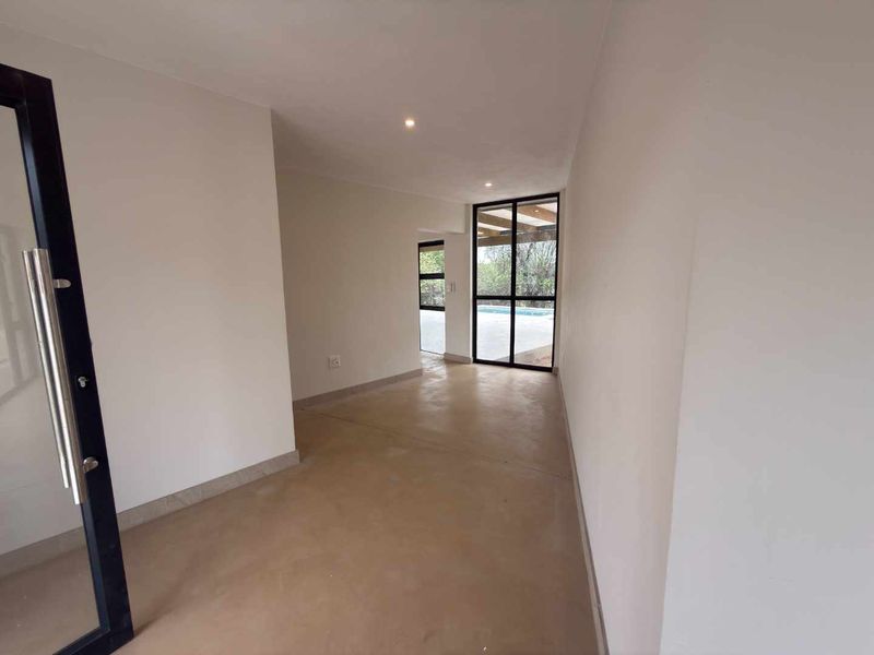 A bright, empty living area featuring polished concrete floors, recessed lighting, and large black-framed glass doors providing access to the outdoor pool area.