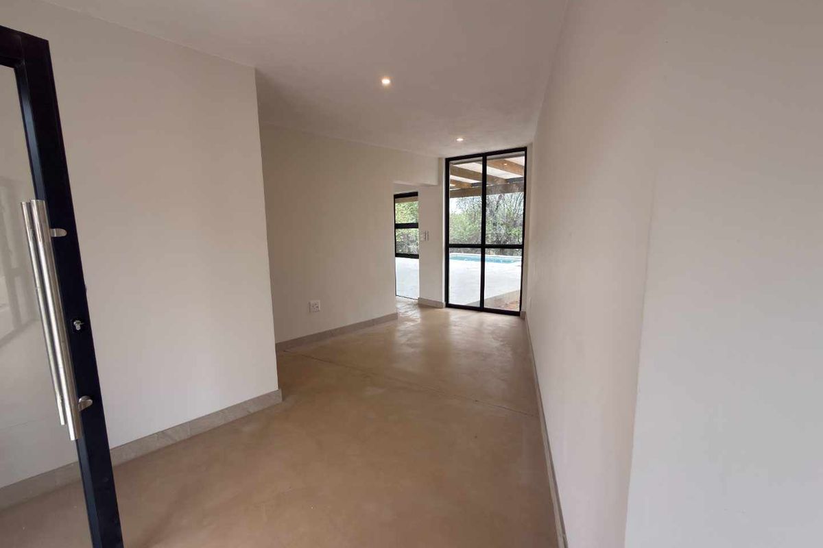 A bright, empty living area featuring polished concrete floors, recessed lighting, and large black-framed glass doors providing access to the outdoor pool area.