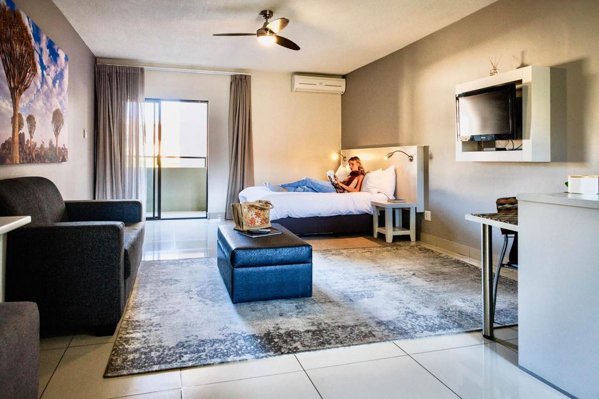 Spacious hotel bedroom featuring tiled flooring, a ceiling fan, split-system air conditioning, and a sliding glass door leading to a private balcony.