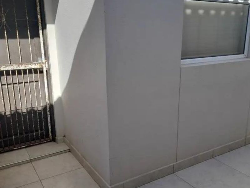 Exterior view of an apartment entrance featuring tiled flooring, a sliding window, and a security gate showing signs of corrosion.
