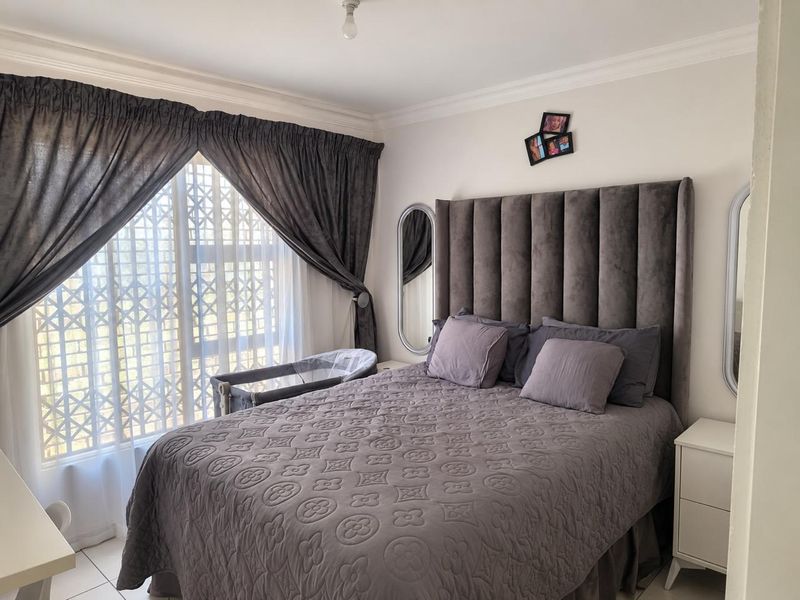 A well-maintained bedroom featuring tiled flooring, crown molding, and a large window fitted with a security gate.