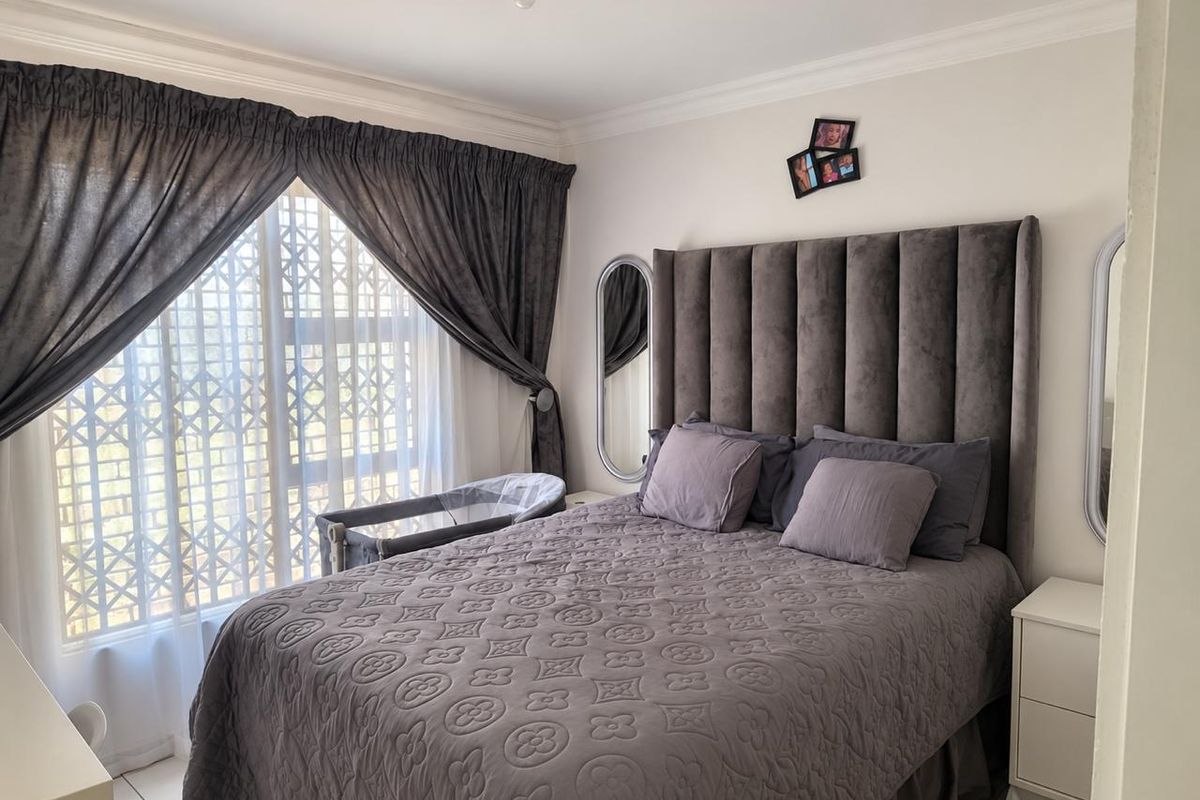 A well-maintained bedroom featuring tiled flooring, crown molding, and a large window fitted with a security gate.